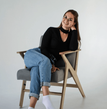 female in blue jeans and black pullover reclining in chair